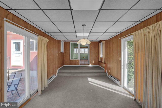 unfurnished dining area featuring a drop ceiling, a baseboard heating unit, wood walls, and carpet flooring