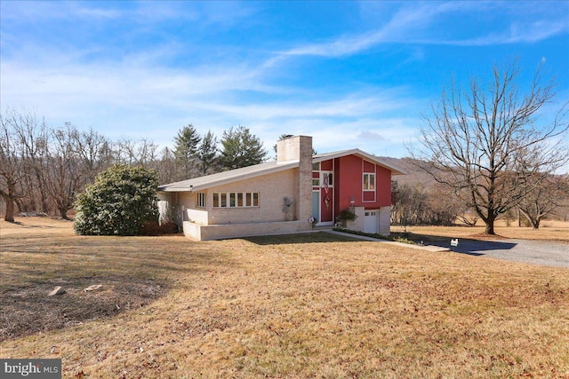 view of home's exterior with driveway, a yard, an attached garage, a chimney, and brick siding