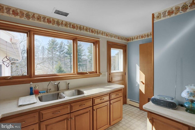 kitchen featuring brown cabinets, baseboard heating, a sink, light countertops, and light floors