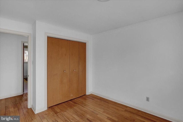 unfurnished bedroom featuring baseboards, light wood-type flooring, and a closet