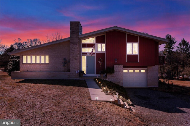 mid-century inspired home with a garage, brick siding, driveway, and a chimney