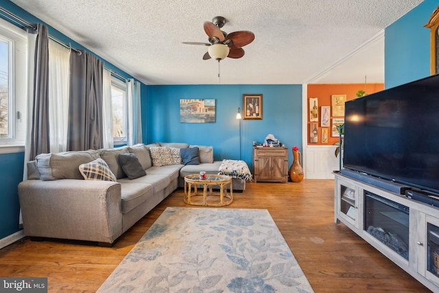 living room featuring a wainscoted wall, a textured ceiling, ceiling fan, and wood finished floors