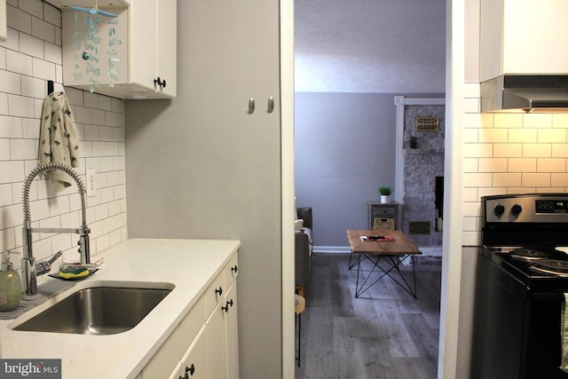 kitchen featuring a sink, wood finished floors, black / electric stove, exhaust hood, and white cabinets