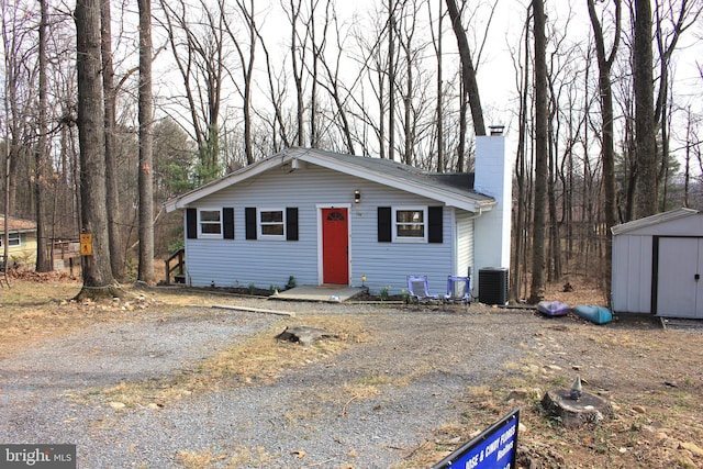 view of front of property featuring central AC unit, a chimney, an outbuilding, driveway, and a storage unit