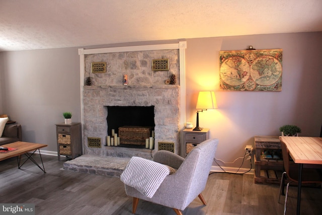 living area featuring visible vents, baseboards, a fireplace, wood finished floors, and a textured ceiling