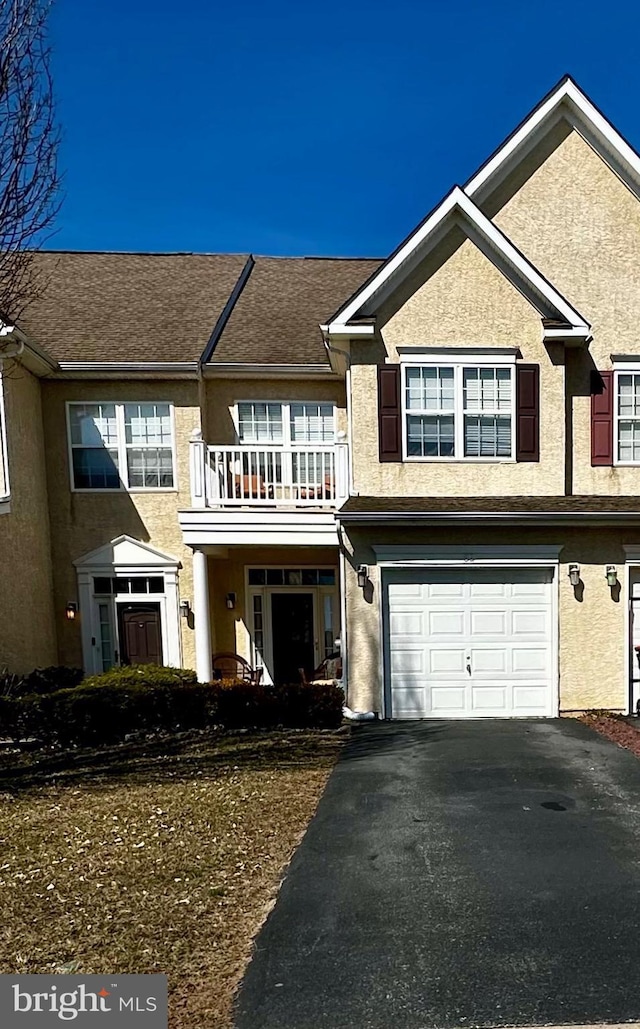 view of property featuring aphalt driveway, a balcony, an attached garage, and stucco siding