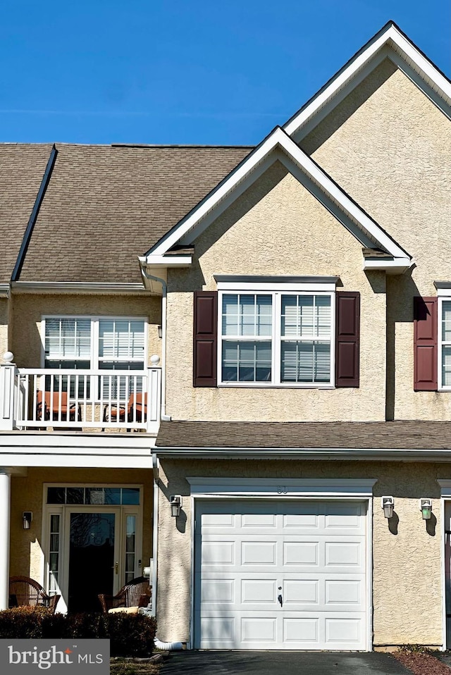 townhome / multi-family property with a balcony, stucco siding, a garage, and roof with shingles