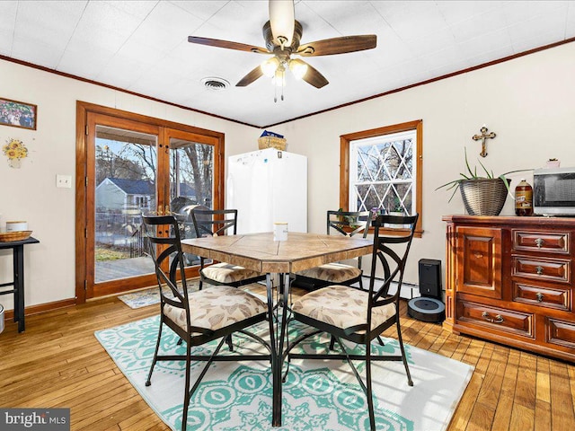 dining room featuring visible vents, a baseboard heating unit, crown molding, and light wood-style floors