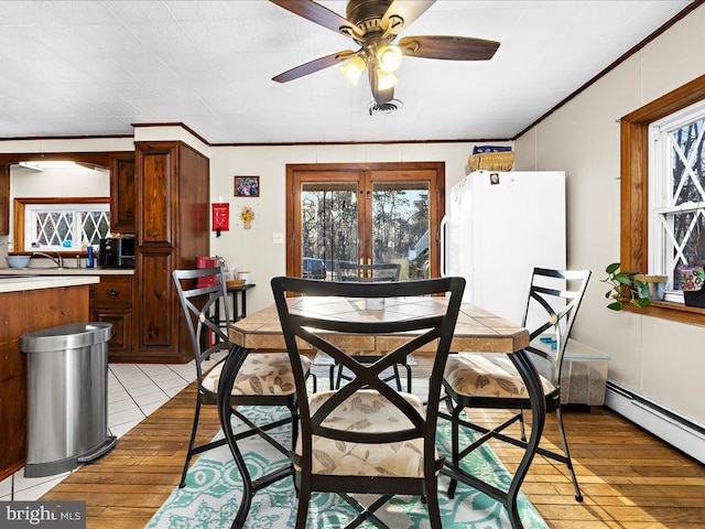 dining space with crown molding, light wood-style floors, visible vents, and baseboard heating