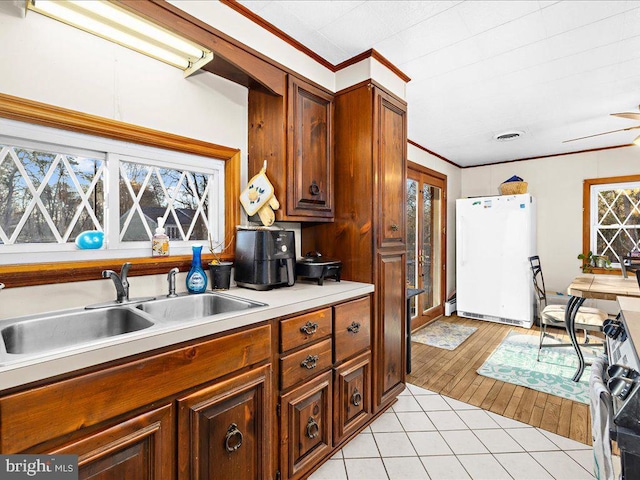 kitchen with a sink, crown molding, light countertops, freestanding refrigerator, and range