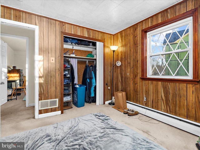 unfurnished bedroom with visible vents, a closet, wood walls, carpet flooring, and baseboard heating