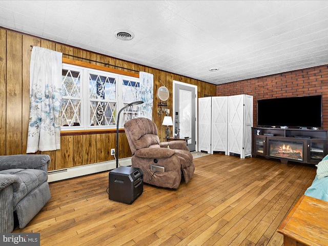 living room with hardwood / wood-style floors, a glass covered fireplace, visible vents, and a baseboard radiator