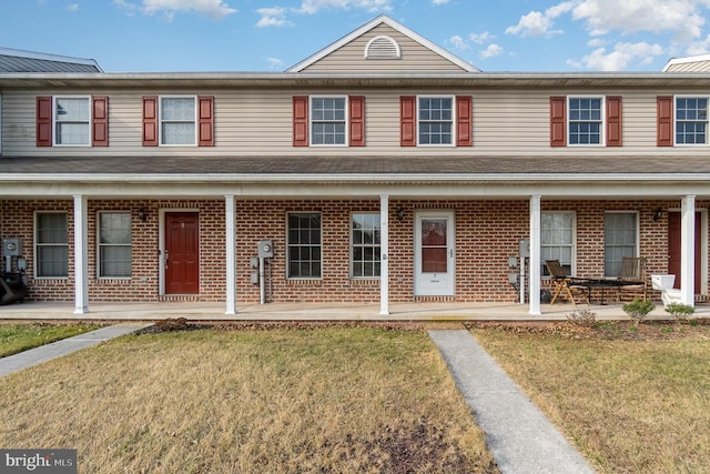 view of property featuring a porch, brick siding, and a front yard