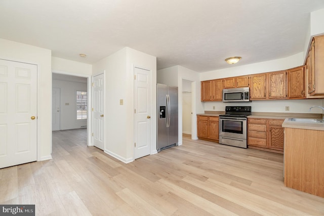 kitchen featuring light countertops, light wood-style flooring, brown cabinets, stainless steel appliances, and a sink