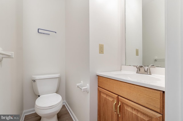 half bath featuring vanity, toilet, wood finished floors, and baseboards