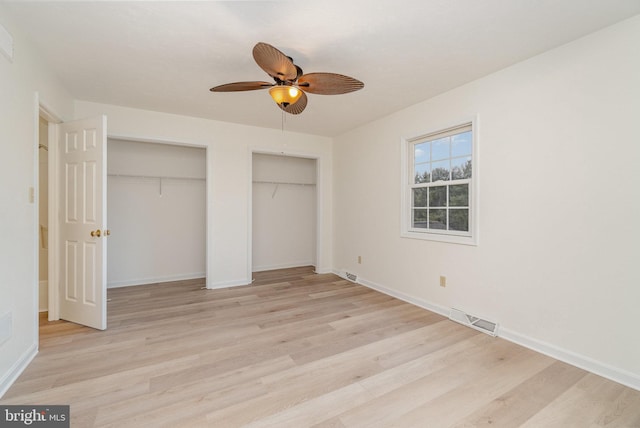 unfurnished bedroom featuring light wood-style flooring, baseboards, visible vents, and two closets