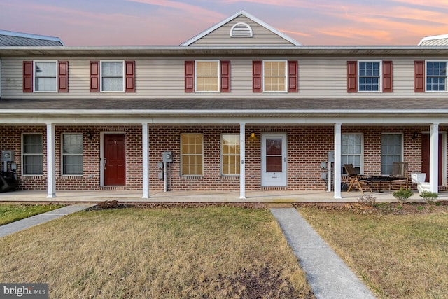 multi unit property with brick siding, a porch, and a front lawn