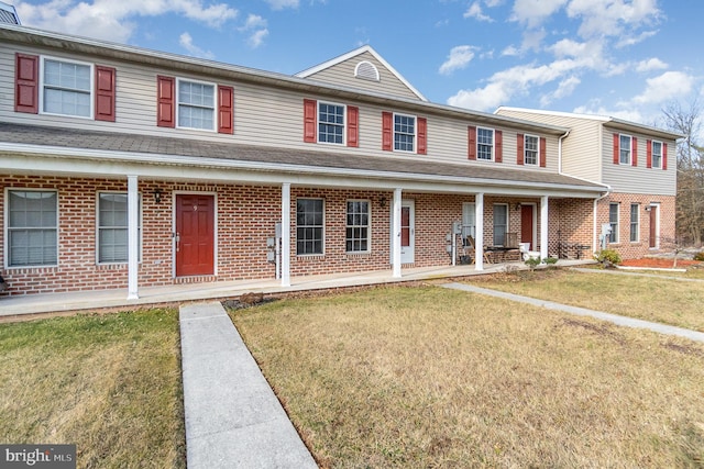 townhome / multi-family property with brick siding, a porch, and a front yard