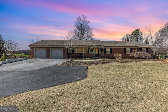 ranch-style house featuring aphalt driveway, a yard, brick siding, and a garage