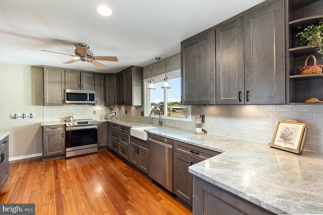 kitchen featuring a sink, open shelves, wood finished floors, stainless steel appliances, and light stone countertops