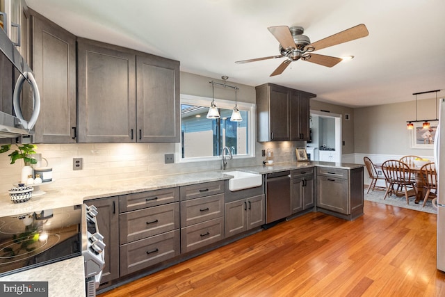 kitchen featuring decorative backsplash, light wood-style flooring, appliances with stainless steel finishes, a peninsula, and a sink