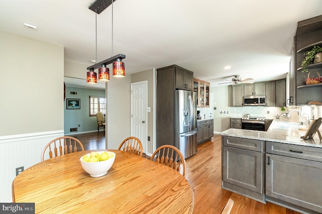 dining area featuring light wood finished floors, a wainscoted wall, and ceiling fan