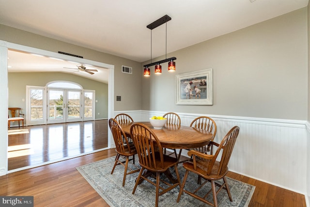 dining room featuring a wainscoted wall, lofted ceiling, wood finished floors, and visible vents