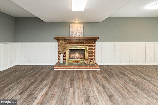 unfurnished living room featuring a wainscoted wall, a brick fireplace, and wood finished floors