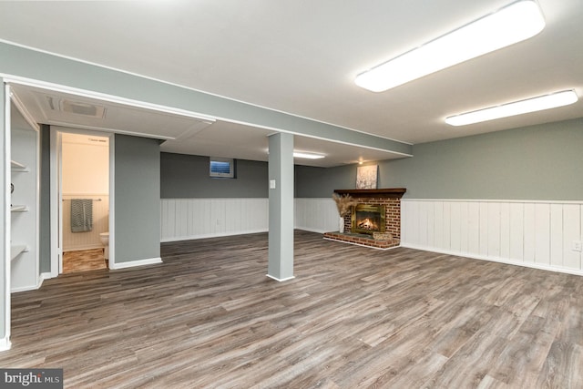 finished basement with a brick fireplace, wood finished floors, and wainscoting