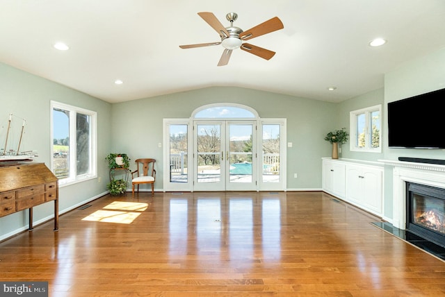 interior space with a glass covered fireplace, vaulted ceiling, wood finished floors, and baseboards