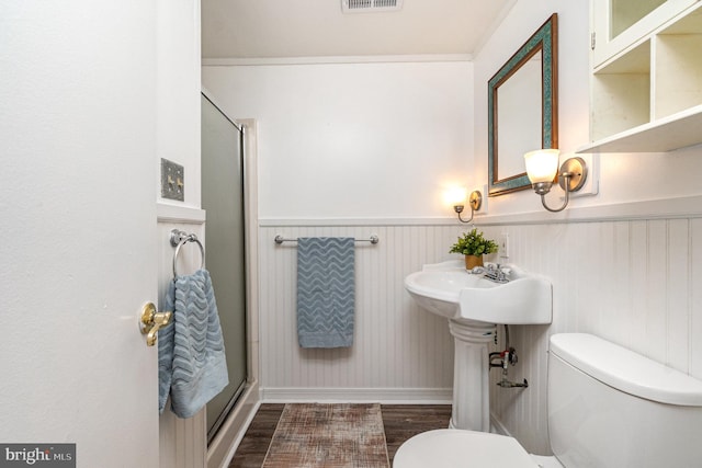 bathroom with a wainscoted wall, a stall shower, toilet, and wood finished floors