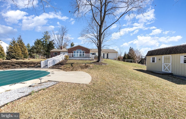 rear view of property with an outbuilding, fence, a shed, a covered pool, and a yard