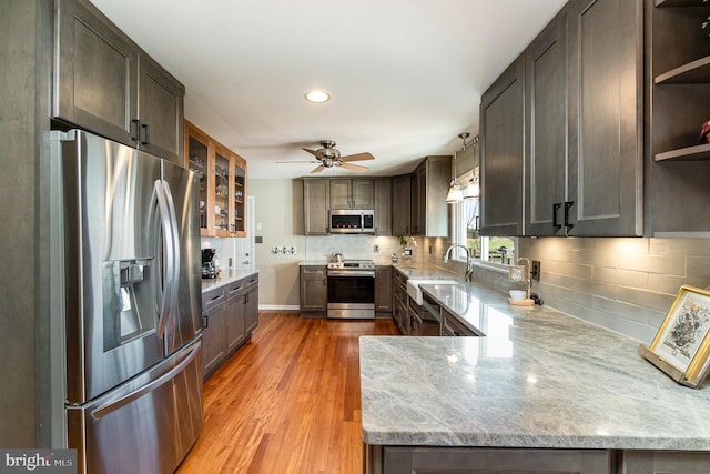 kitchen with backsplash, light wood-style flooring, appliances with stainless steel finishes, and light stone countertops