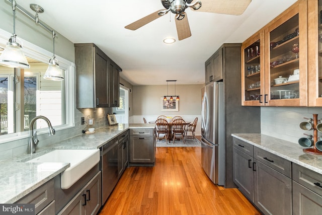 kitchen with light stone counters, light wood-style flooring, stainless steel appliances, a sink, and decorative light fixtures