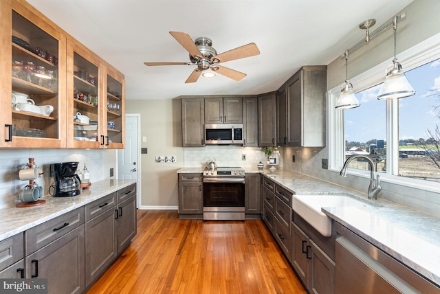 kitchen with light stone countertops, appliances with stainless steel finishes, wood finished floors, and a sink