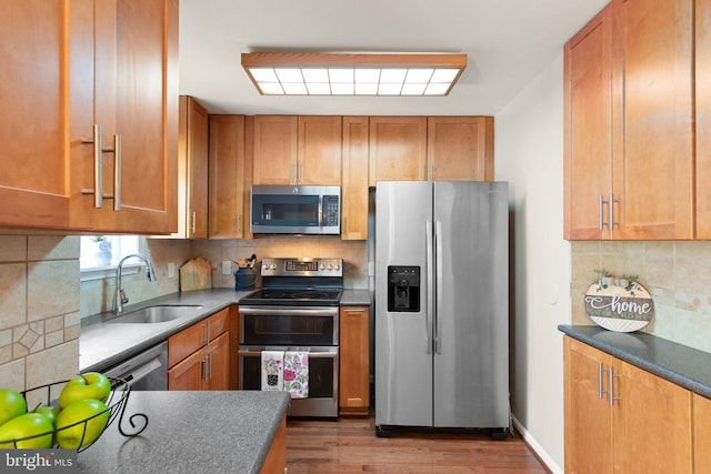 kitchen featuring tasteful backsplash, brown cabinets, appliances with stainless steel finishes, wood finished floors, and a sink