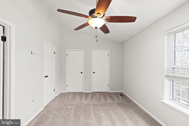 unfurnished bedroom featuring two closets, baseboards, lofted ceiling, light carpet, and a ceiling fan