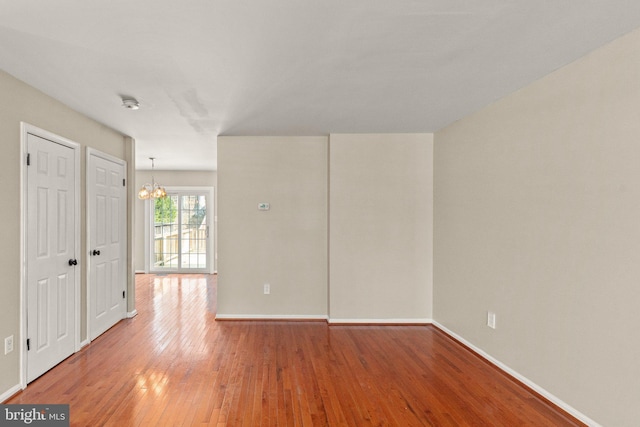 spare room featuring baseboards, light wood-style floors, and an inviting chandelier