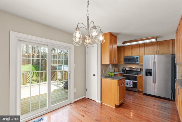 kitchen featuring light wood-style flooring, dark countertops, backsplash, appliances with stainless steel finishes, and brown cabinetry