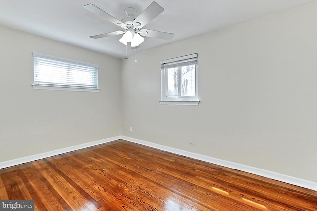 spare room with a ceiling fan, a healthy amount of sunlight, baseboards, and dark wood-style flooring