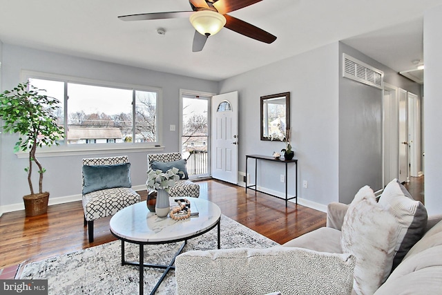 living room with ceiling fan, visible vents, baseboards, and wood finished floors