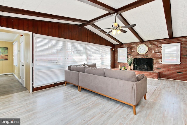 living room with a ceiling fan, wood finished floors, brick wall, a fireplace, and vaulted ceiling with beams