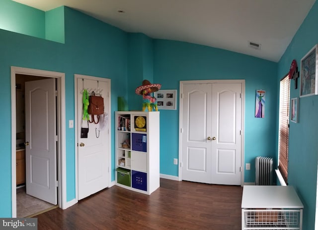 unfurnished bedroom featuring visible vents, dark wood-style floors, baseboards, radiator, and lofted ceiling