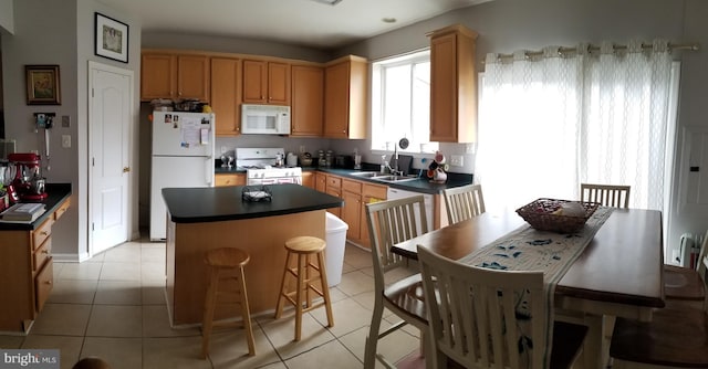 kitchen with a sink, dark countertops, a center island, white appliances, and light tile patterned floors