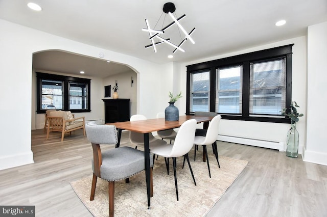 dining space featuring arched walkways, baseboards, a baseboard heating unit, and light wood-style floors