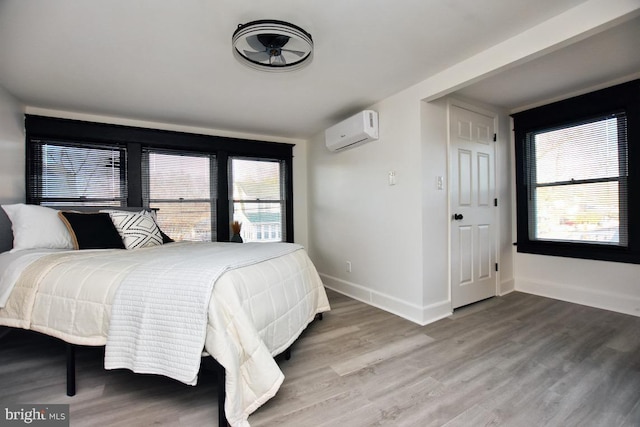 bedroom featuring an AC wall unit, baseboards, and wood finished floors