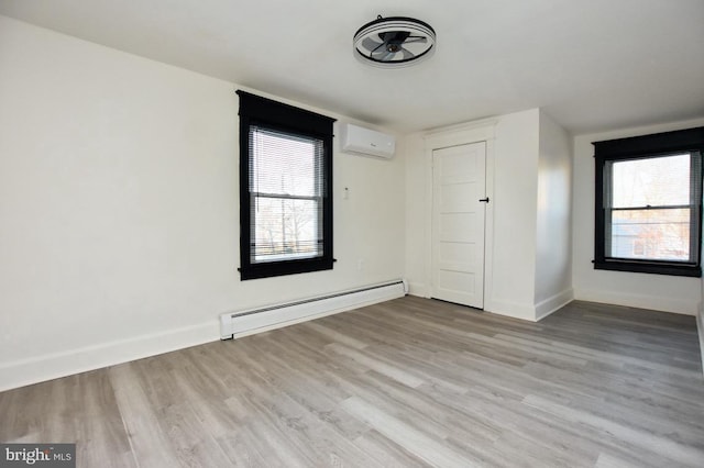 unfurnished room featuring a baseboard heating unit, baseboards, an AC wall unit, and wood finished floors