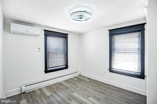 spare room featuring a baseboard heating unit, wood finished floors, baseboards, and a wall mounted AC