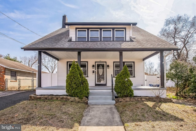 bungalow with a chimney, covered porch, a shingled roof, and fence