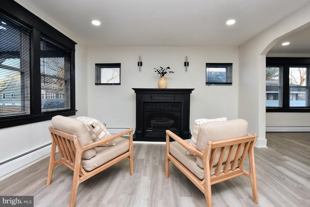 living area with a baseboard radiator, arched walkways, wood finished floors, and a fireplace